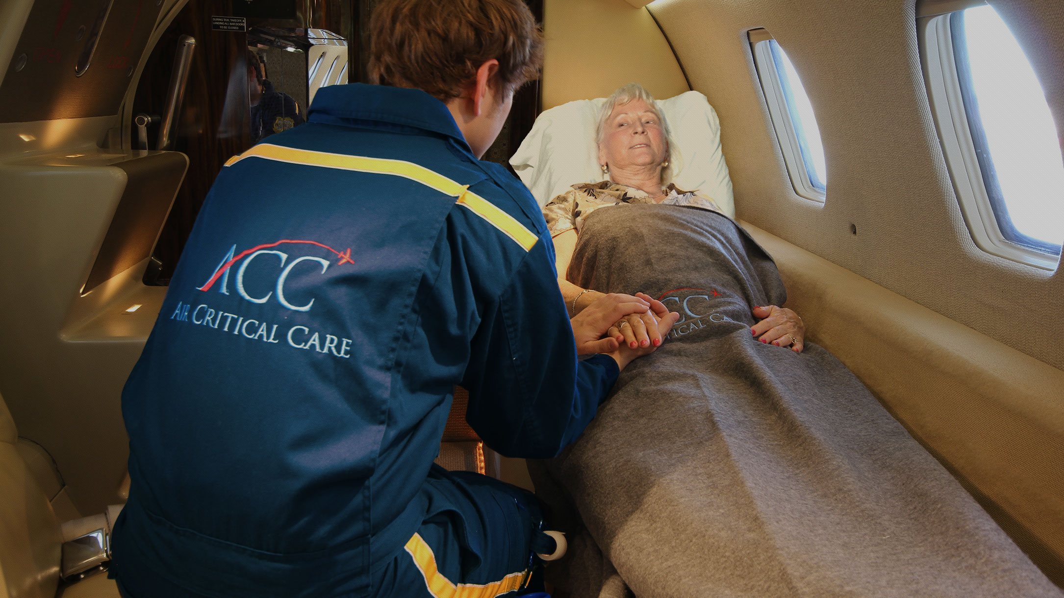 Air Critical Care flight nurse holding a patient's hand aboard a private air ambulance
